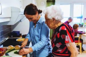 Side View Of Senior Woman Looking At Daughter Cutting Zucchini In Kitchen