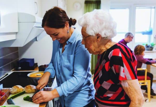 Side View Of Senior Woman Looking At Daughter Cutting Zucchini In Kitchen