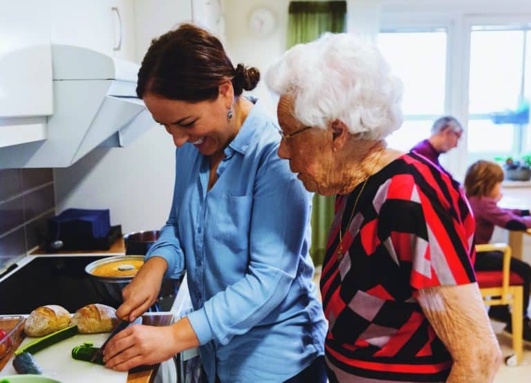 Side View Of Senior Woman Looking At Daughter Cutting Zucchini In Kitchen