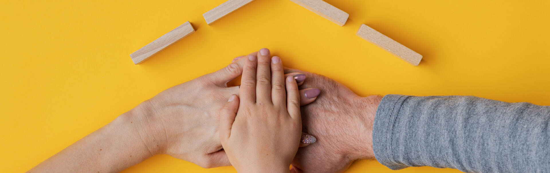 Family Stacking Their Hand On Yellow Background With Roof Made O