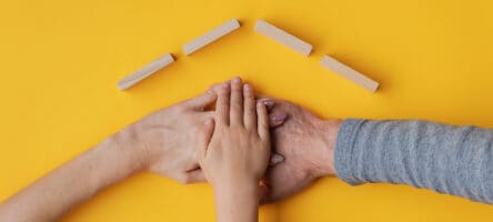 Family Stacking Their Hand On Yellow Background With Roof Made O