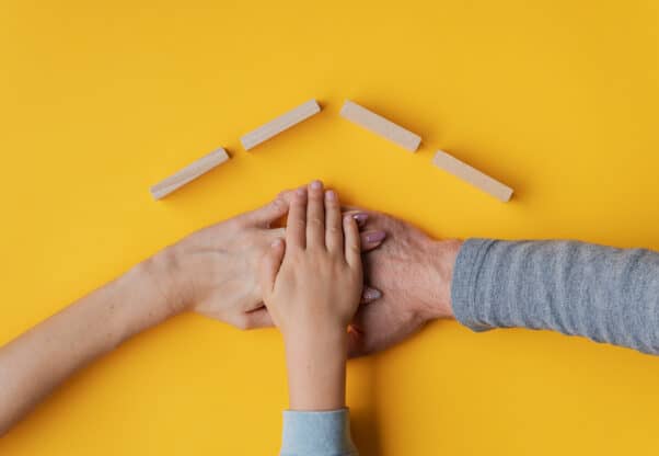 Family Stacking Their Hand On Yellow Background With Roof Made O