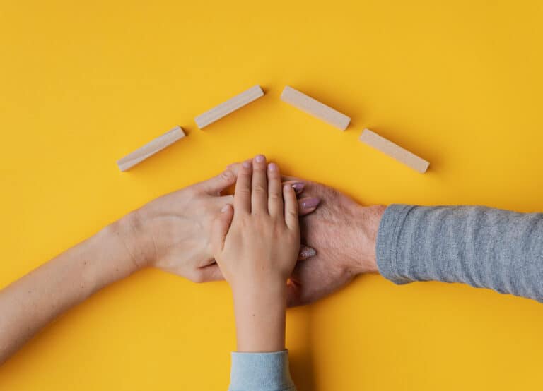 Family Stacking Their Hand On Yellow Background With Roof Made O