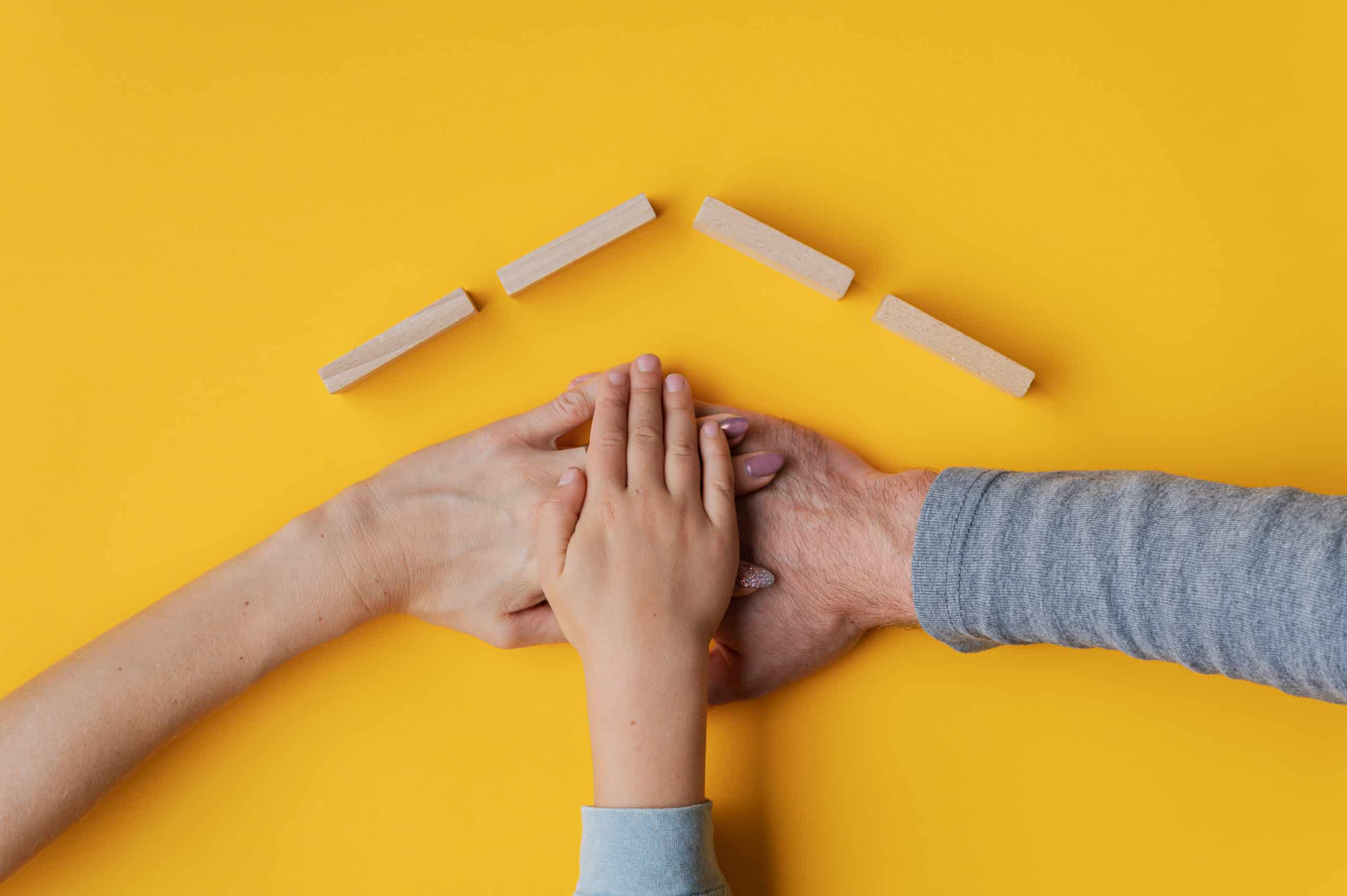 Family Stacking Their Hand On Yellow Background With Roof Made O