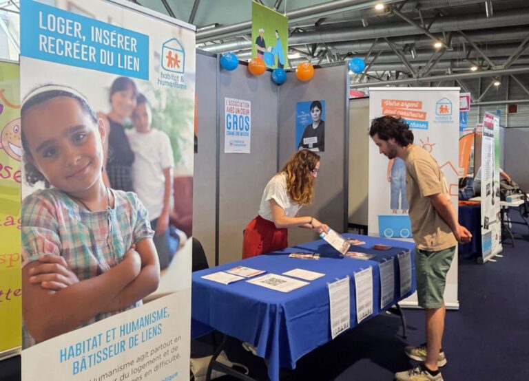 Stand d'Habitat et Humanisme à Explor'Assos à Mulhouse. Une salariée est entrain de renseigner un visiteur à l'aide d'une plaquette d'informations de l'association.